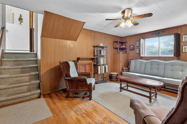 Living area featuring a ceiling fan, wooden walls, light wood-style floors, and stairs | Image 8
