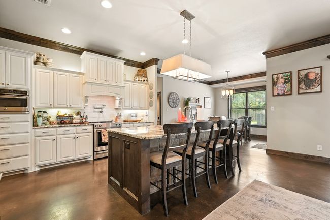 Kitchen featuring appliances with stainless steel finishes, concrete floors, tasteful backsplash, ornamental molding, and a kitchen breakfast bar | Image 6