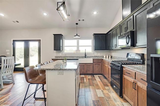 Kitchen with light stone countertops, stainless steel appliances, a center island, and hardwood / wood-style floors | Image 13