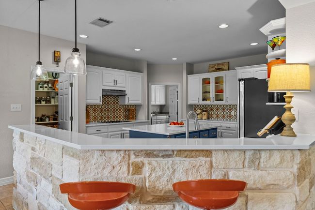 The upgraded cabinets include accent rain glass doors, complemented by pendant lights, stone on the breakfast bar, and high-end stainless appliances | Image 11