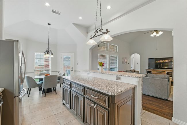 Kitchen featuring freestanding refrigerator, arched walkways, light tile patterned floors, a center island, and pendant lighting | Image 13