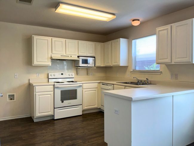 Kitchen with light countertops, white appliances, white cabinetry, a peninsula, and dark wood-style floors | Image 4