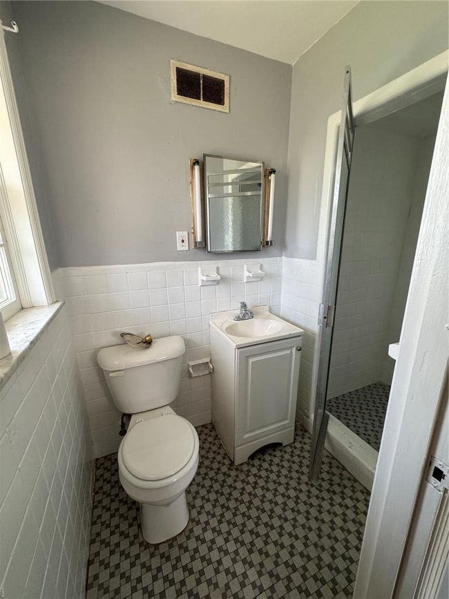 Bathroom with tile walls, toilet, a shower stall, visible vents, and wainscoting | Image 16