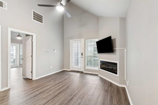 Unfurnished living room featuring ceiling fan, high vaulted ceiling, wood finished floors, and a glass covered fireplace | Image 5