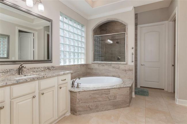 This bathroom features a modern design with a spacious soaking tub, granite countertops, dual sinks, and ample natural light through glass block windows. Neutral tones and elegant fixtures create a serene, spa-like atmosphere. | Image 29