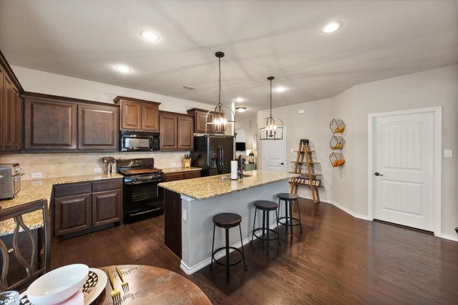 Kitchen with an inviting chandelier, black appliances, a breakfast bar, decorative backsplash, and dark wood-style floors | Image 14