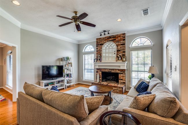 Living room featuring ceiling fan, light wood finished floors, crown molding, and a fireplace | Image 6