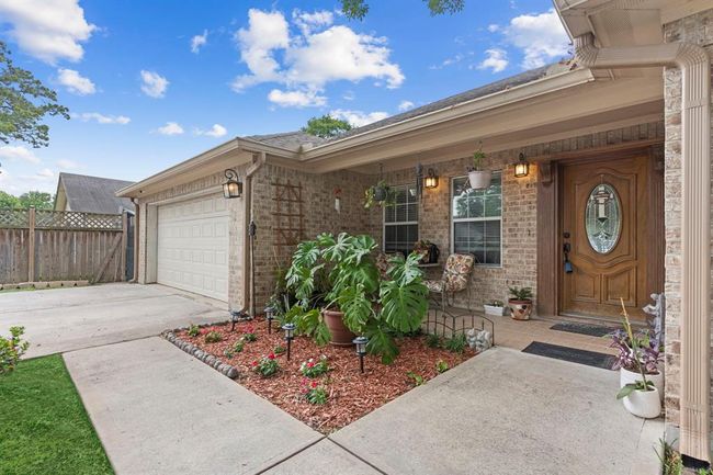 This is a well-maintained single-story brick home featuring an attached garage, a welcoming front porch with decorative lighting, and a landscaped entryway. | Image 6