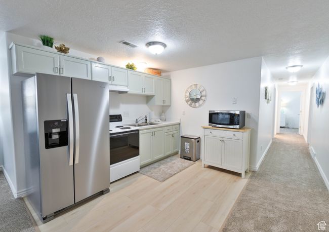 Kitchen with appliances with stainless steel finishes, a sink, under cabinet range hood, a textured ceiling, and light countertops | Image 42
