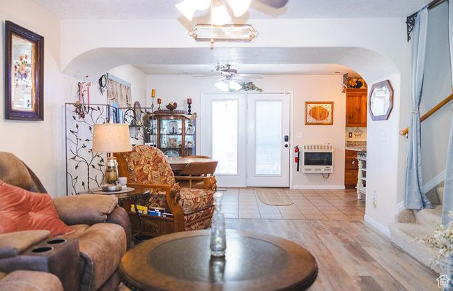 Living area with heating unit, arched walkways, ceiling fan, stairway, and light wood-style floors | Image 7