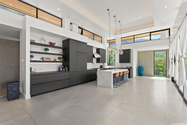 High-end Thermador stainless steel appliances in the kitchen, including a refrigerator, gas range, industrial hood fan, built-in microwave, dishwasher, and a dual-zone wine refrigerator. Bookmatched quarts waterfall countertop and black Lapitec countertops along the wall. *Virtually removed dining table to show space better* | Image 7