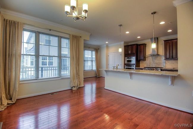 Kitchen with wall chimney range hood, wood finished floors, a breakfast bar, ornamental molding, and backsplash | Image 4