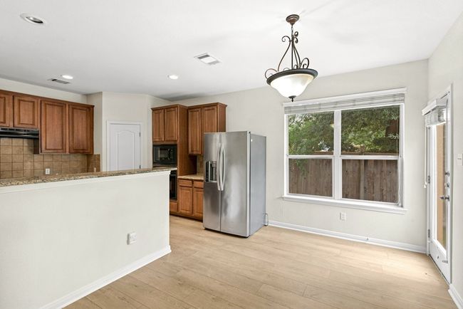Kitchen with black appliances, brown cabinetry, under cabinet range hood, decorative backsplash, and pendant lighting | Image 13