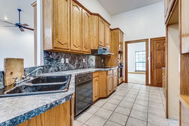 Kitchen with black appliances, under cabinet range hood, ceiling fan, decorative backsplash, and light tile patterned floors | Image 9