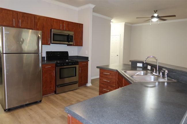 Kitchen with stainless steel appliances, a sink, dark countertops, light wood-type flooring, and ornamental molding | Image 6