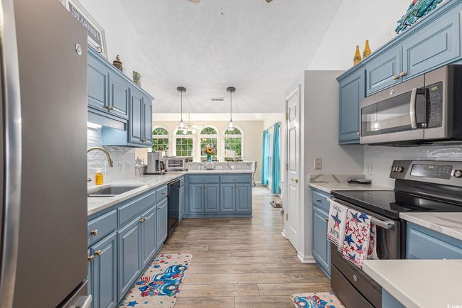 Kitchen featuring appliances with stainless steel finishes, a sink, blue cabinetry, light countertops, and decorative backsplash | Image 17