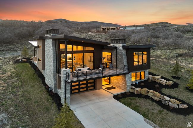 Back of house at dusk with an attached garage, a balcony, a mountain view, and concrete driveway | Image 6