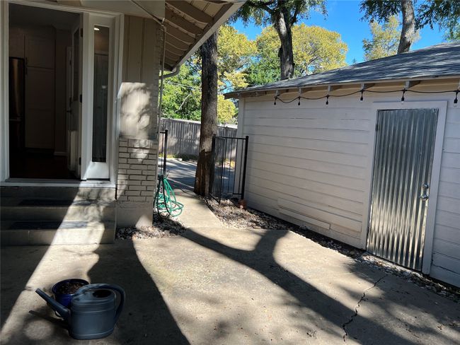 View of side of home featuring a patio area, roof with shingles, an outbuilding, brick siding, and entry steps | Image 24