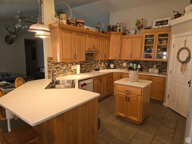 Kitchen with a sink, light countertops, a ceiling fan, stainless steel dishwasher, and a breakfast bar area | Image 24