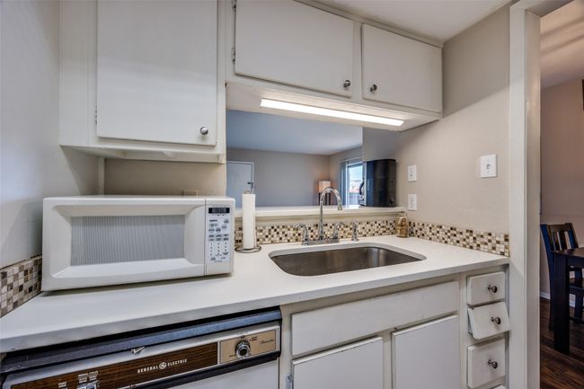 Kitchen with white microwave, a sink, dishwashing machine, and light countertops | Image 10