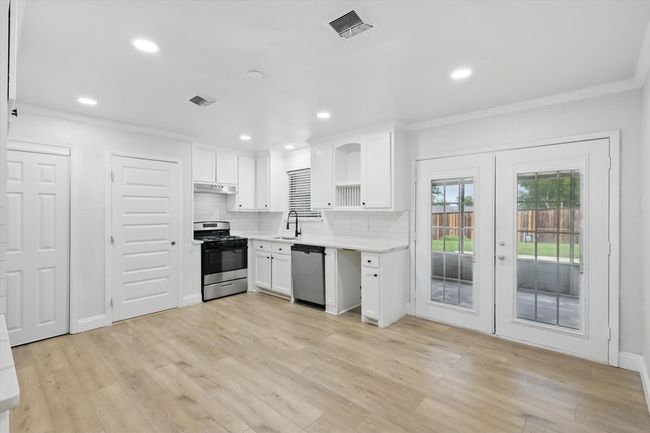 Kitchen with stainless steel appliances, under cabinet range hood, open shelves, french doors, and a sink | Image 6