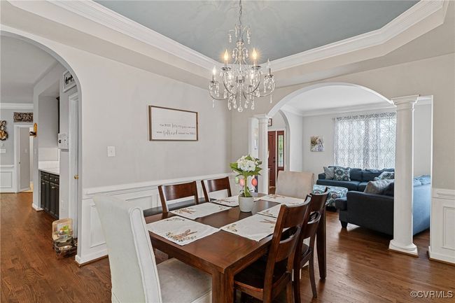 Dining area featuring arched walkways, an inviting chandelier, wainscoting, dark wood-style floors, and crown molding | Image 20