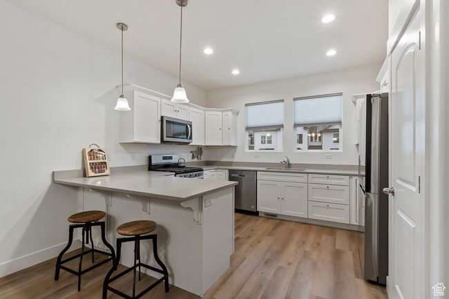 Kitchen with stainless steel appliances, decorative light fixtures, kitchen peninsula, and white cabinets | Image 9