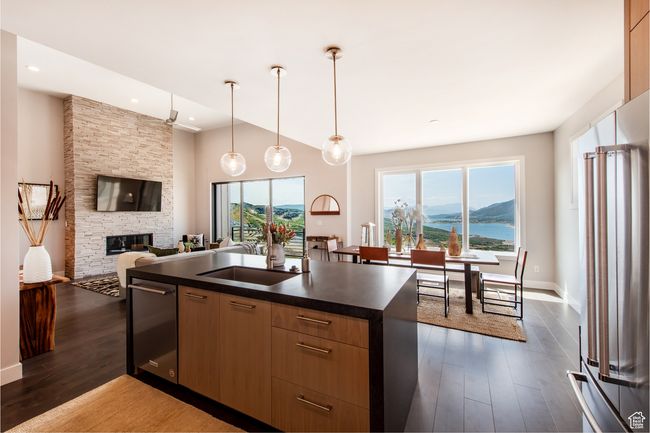 Kitchen featuring dark hardwood / wood-style floors, an island with sink, pendant lighting, high quality fridge, and a fireplace | Image 7