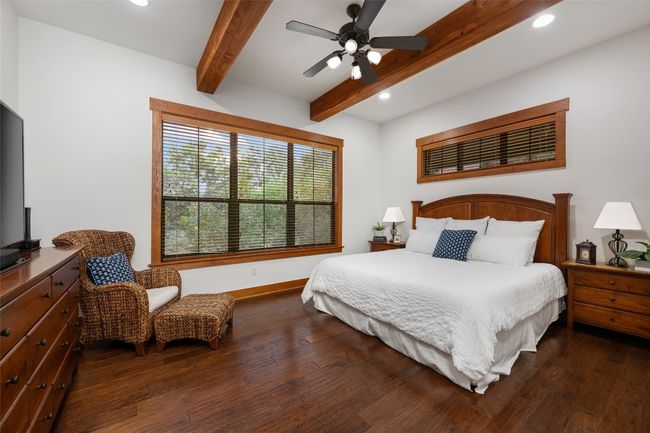 The spacious primary bedroom offers a peaceful retreat with exposed wood beams, large windows that provide natural light. | Image 12