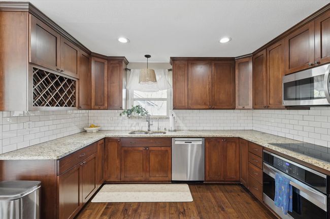 Kitchen featuring stainless steel appliances, dark wood-type flooring, light stone counters, backsplash, and recessed lighting | Image 10