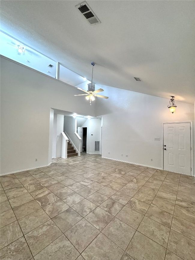 Unfurnished living room featuring vaulted ceiling, a ceiling fan, and stairs | Image 5