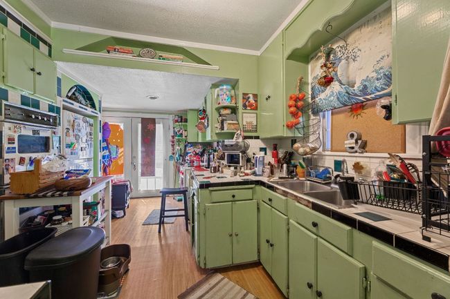 Kitchen featuring a sink, light wood-style flooring, a textured ceiling, and tile counters | Image 16