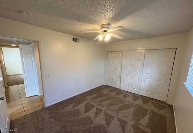 Unfurnished bedroom featuring carpet floors, a textured ceiling, a closet, ceiling fan, and tile patterned floors | Image 7
