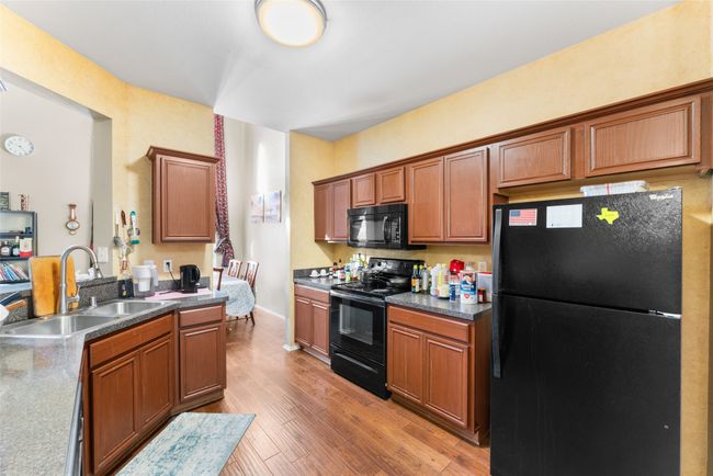 Kitchen featuring dark countertops, a sink, light wood-style floors, black appliances, and brown cabinetry | Image 10