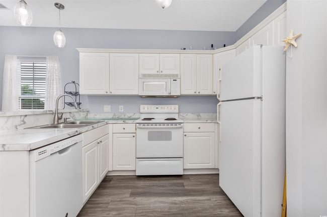 Kitchen featuring white appliances, a sink, white cabinetry, light countertops, and dark wood finished floors | Image 5