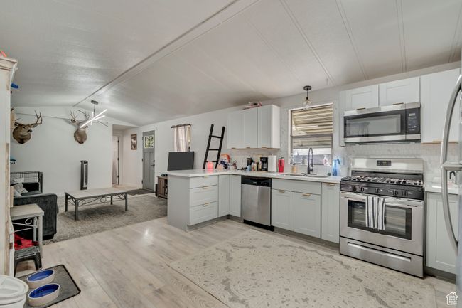 Kitchen with stainless steel appliances, a peninsula, a sink, light wood-type flooring, and backsplash | Image 4