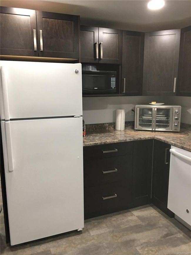 Kitchen with dark brown cabinetry, white appliances, a toaster, and dark stone counters | Image 26