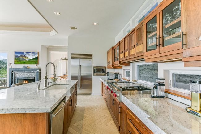 Kitchen with built in appliances, brown cabinetry, light stone counters, glass insert cabinets, and recessed lighting | Image 10