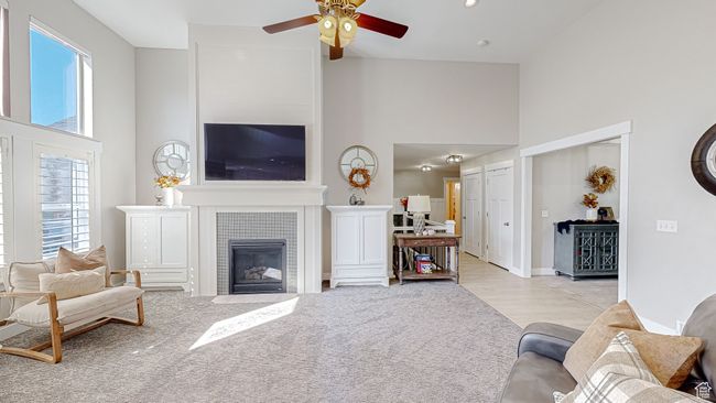 Living area with baseboards, a high ceiling, light carpet, a tile fireplace, and ceiling fan | Image 6