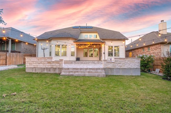 Back of house with solar panels, a fenced backyard, roof with shingles, a patio area, and stone siding | Image 38