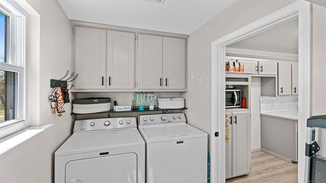 Clothes washing area featuring light wood-type flooring, washing machine and clothes dryer, and cabinet space | Image 37
