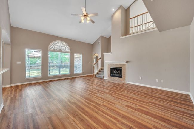 Unfurnished living room with light wood-style flooring, baseboards, high vaulted ceiling, and a ceiling fan | Image 5