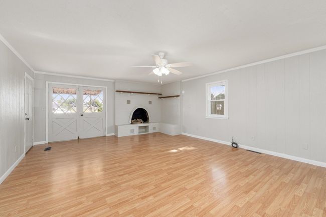 Unfurnished living room featuring ornamental molding, light wood-style floors, a ceiling fan, a brick fireplace, and plenty of natural light | Image 9