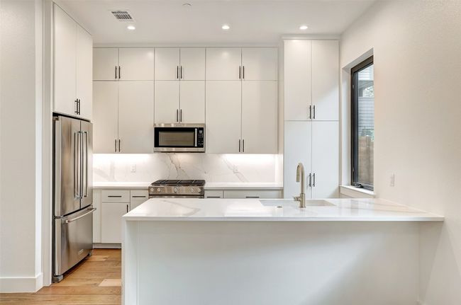 Kitchen with appliances with stainless steel finishes, a sink, light wood finished floors, a peninsula, and decorative backsplash | Image 10