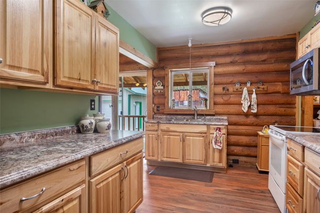 Kitchen with white range with electric cooktop, stainless steel microwave, log walls, dark wood-style floors, and stone countertops | Image 38