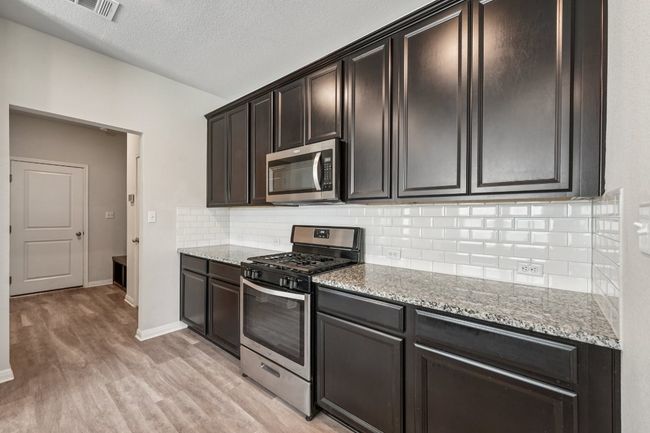 Kitchen with stainless steel appliances, light wood-style floors, light stone counters, decorative backsplash, and a textured ceiling | Image 6