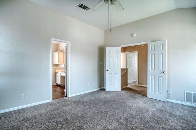 Unfurnished bedroom featuring carpet flooring, baseboards, vaulted ceiling, ensuite bathroom, and ceiling fan | Image 5