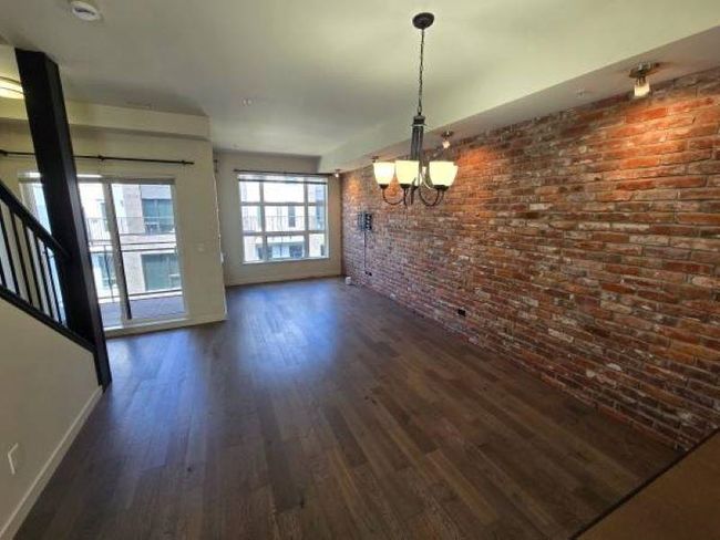Unfurnished dining area featuring a chandelier, dark wood-type flooring, brick wall, baseboards, and stairway | Image 7