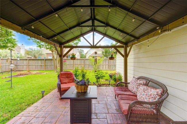 This inviting backyard space features a covered patio with cozy seating, perfect for relaxing. It overlooks a well-maintained lawn and garden, enclosed by a wooden fence for privacy. Ideal for outdoor gatherings. | Image 6
