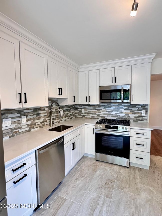 Marble countertop and gorgeous backsplash, black hardware complete this great kitchen. | Image 6